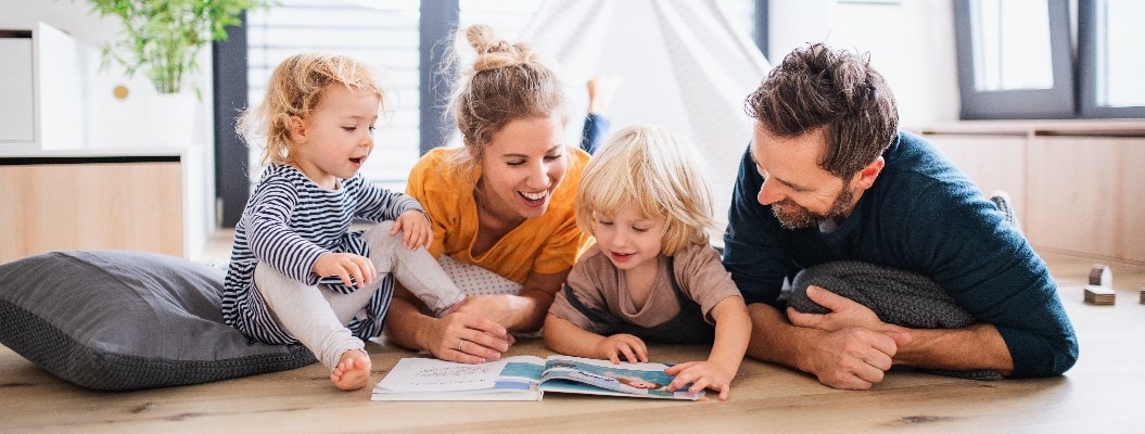 Junge Familie mit zwei kleinen Kindern beim Lesen eines Buches.