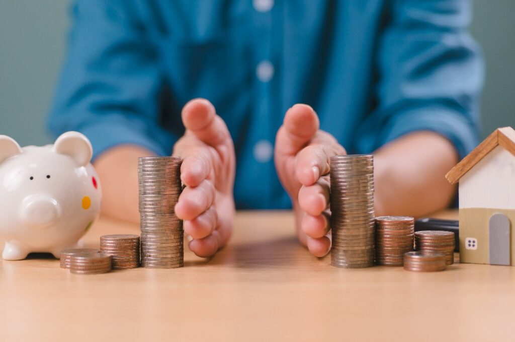 Scheidungsrecht und Erbe Trennung Konzept. Hand getrennt sparen Geld, Finanz-, Haus-Darlehen, Schulden mit Sparschwein und Holzhaus. Bankgeschäft Investition. Mann trennen Stapel Münze auf dem Tisch